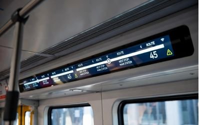 Slim bar LCD display inside a bus or metro showing real-time route and stop information.