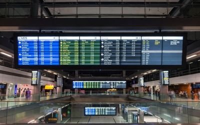 Ultra-wide bar LCD information display in a train station or airport showing schedules and directions.