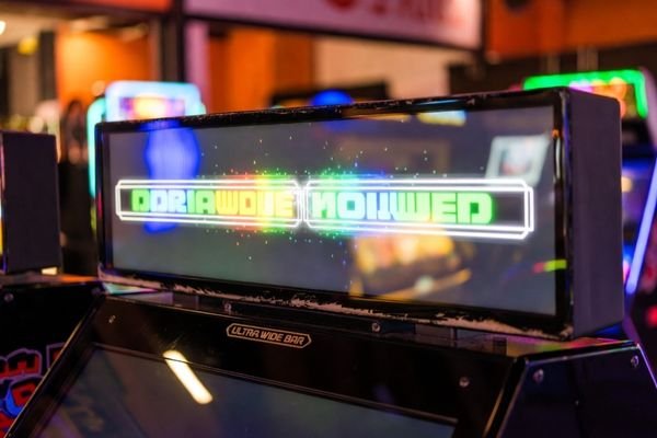 Ultra-wide bar display mounted on top of an arcade gaming machine showing dynamic status graphics.