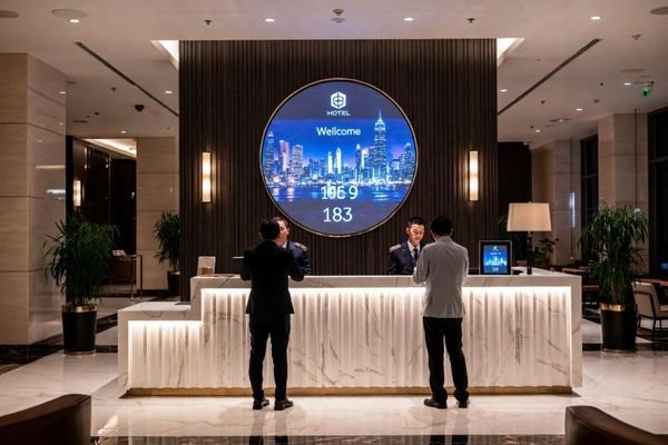 A hotel lobby reception area with a large round LCD display module on the wall showing a welcome animation and branding visuals
