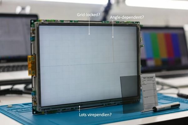Quality lab inspection of a large LCD display module showing a thin vertical line defect on a gray test pattern with tools for angle and temperature checks.