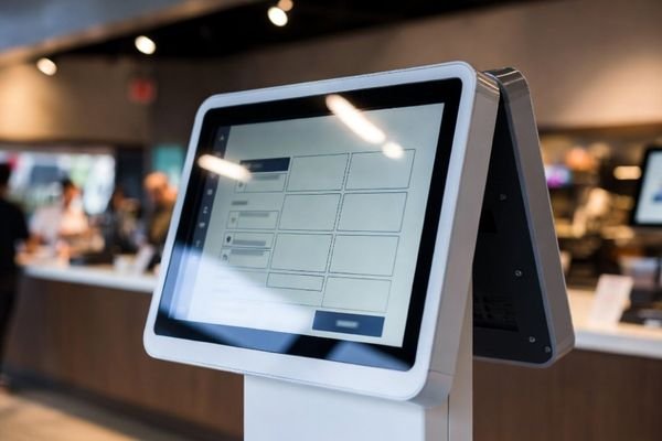 Self-order kiosk in a bright fast-food restaurant with a large touchscreen display designed for high readability.