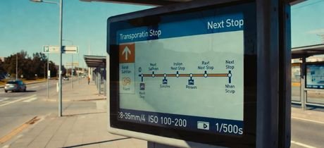Outdoor transit passenger information terminal in bright sunlight with a large display showing route and next-stop information