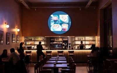 A modern café interior with a large round LCD display module on the wall showing food and drink animations