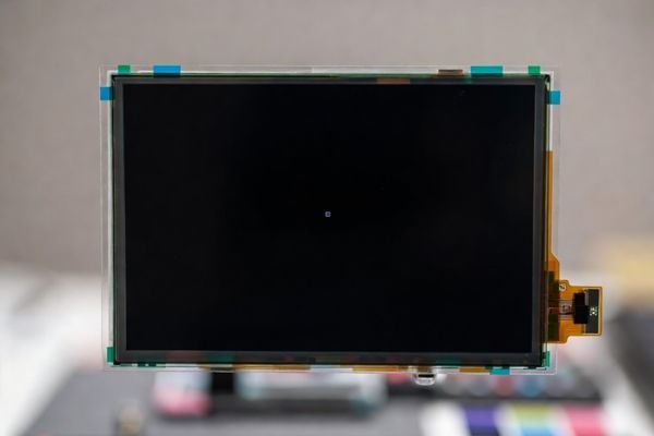 LCD display module on a controlled inspection jig showing a black test pattern with a single bright pixel, alongside a zone overlay and measurement tools for repeatable pixel-defect acceptance.