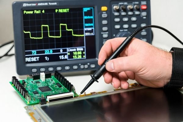 Engineer probing RESET test point near LCD connector while viewing oscilloscope waveforms