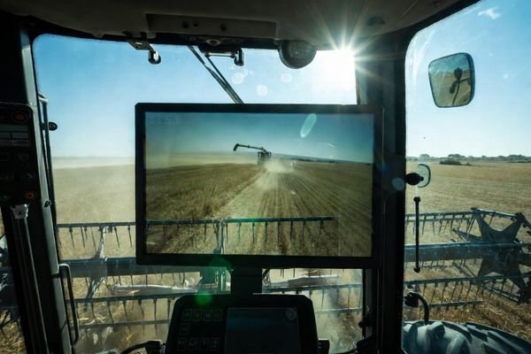 An image of a combine harvester working in a dusty field under bright sunlight